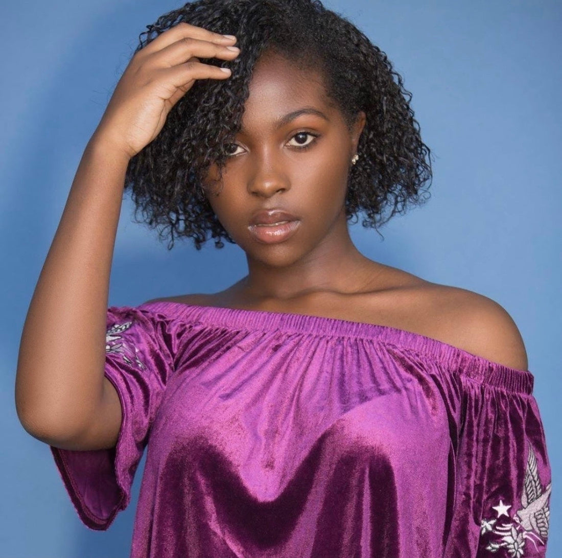 Young woman with natural curly hair wearing an off-shoulder purple top.