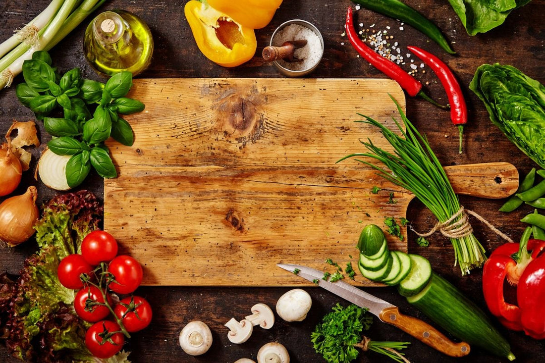 Wooden cutting board surrounded by fresh vegetables and herbs.