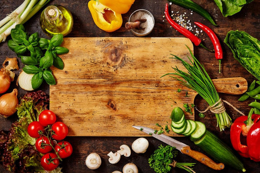 Wooden cutting board surrounded by fresh vegetables and herbs.